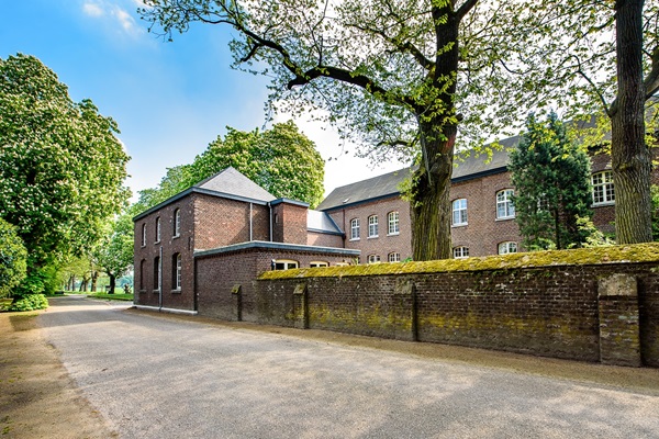 Abdij Lilbosch gezien vanaf de zijkant met een muur vol met mos en bomen die in bloei staan.