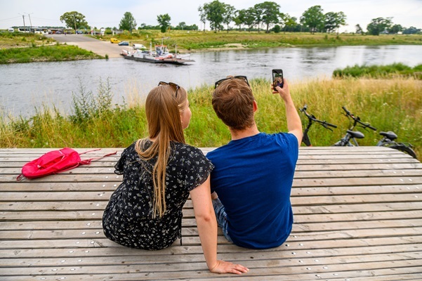 Een stel maakt een selfie terwijl ze uitkijken over de Maas, met fietsen op de achtergrond.