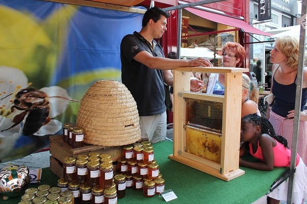 Marktkraam op de Sjoemelmert in Roermond met een imker die bezoekers uitlegt over bijen, honingpotten en een bijenkorf.