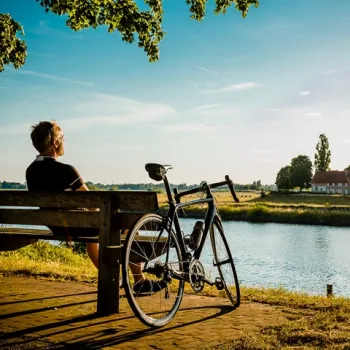 Fietser rust op een bankje aan het water in Hart van Limburg, met uitzicht over het landschap bij avondlicht