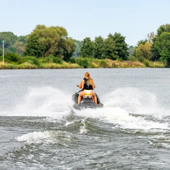 Een vrouw op een waterscooter scheurt over het water van de Maasplassen, omringd door groen.