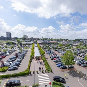 Overzicht van parkeerterrein en parkeergarage bij Designer Outlet Roermond op een zonnige dag.