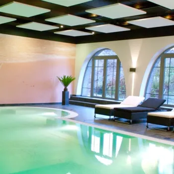 Hotel met luxe binnenzwembad, ligstoelen en grote ramen met uitzicht op het groen.